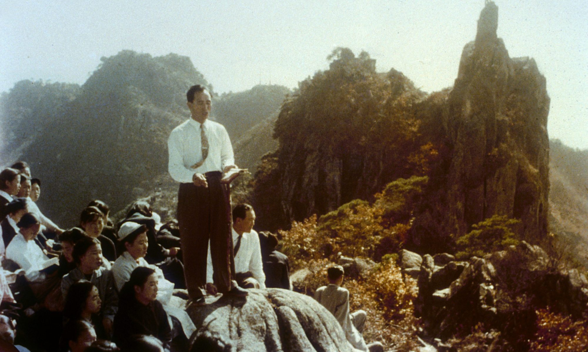 Sun Myung Moon teaching on a mountainside surrounded by members
