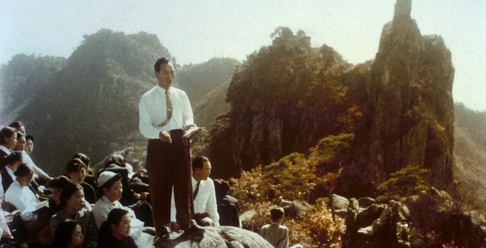 Sun Myung Moon teaching on a mountainside surrounded by members